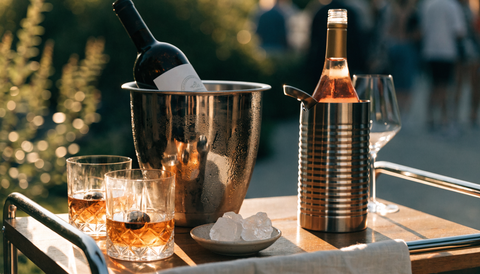 Outdoor bar cart with a stainless ice bucket, bottle chiller, and whiskey glasses with chilling stones set up for a summer party